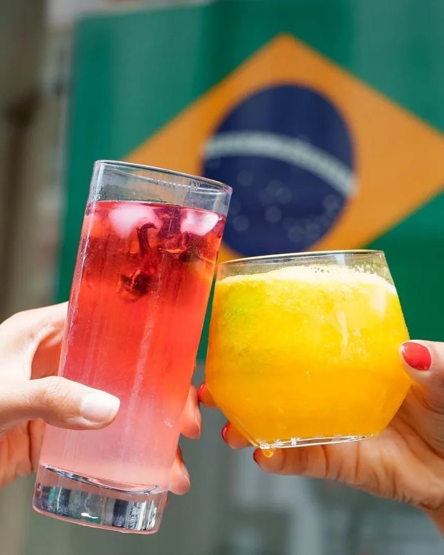 Photo de deux amis qui trinquent avec une caïpifruta et un verre rose devant le drapeau du Brésil chez Snack Brasil, le meilleur restaurant pour fêter son anniversaire autour d'une caïpirinha à Lyon, Vaise, Lyon 9